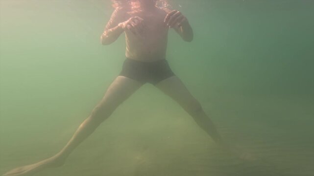Man swimming and floating underwater in a dark, opaque lake. Sunlight filtering through the water creating a hazy effect