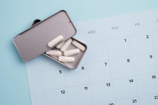 White medical capsules placed directly on a light blue monthly calendar. Health management, medication adherence, treatment scheduling, and tracking a daily medical routine.