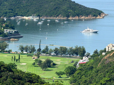 Luxury yacht anchored in a bay with a golf course and lush green hills