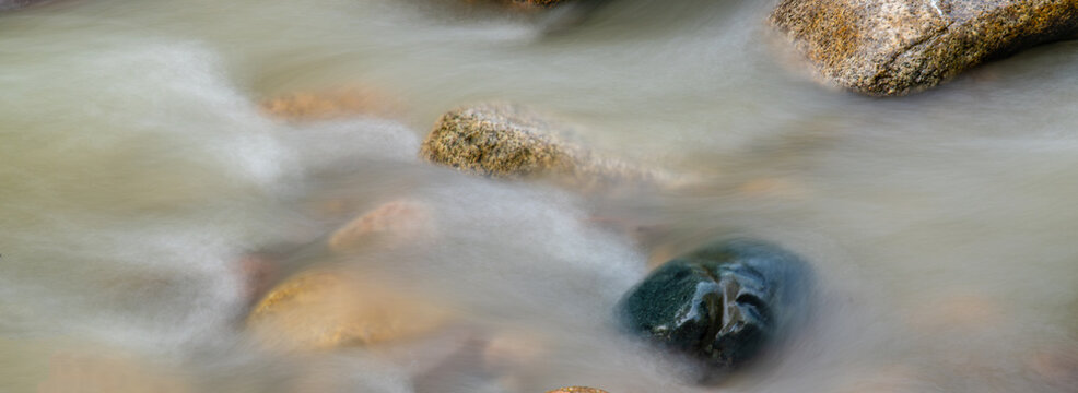 Long exposure shot of smooth flowing river water around large stones with silky effect