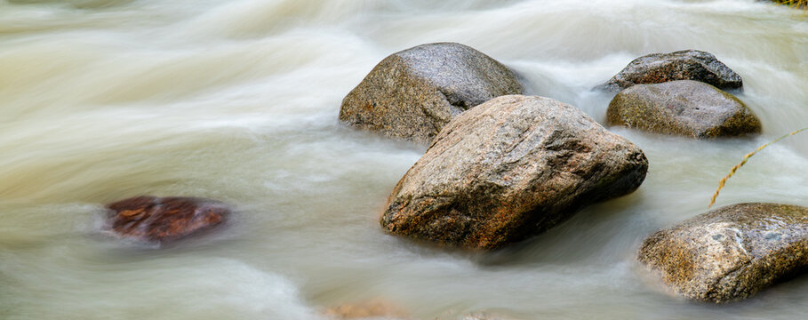 Long exposure shot of smooth flowing river water around large stones with silky effect, nature landscape photography concept