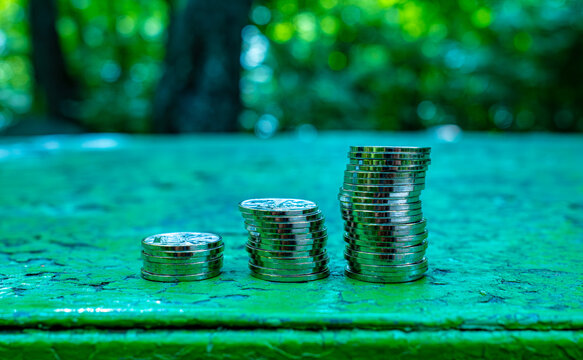 Stack of silver coins on green surface in park with bokeh background, savings and financial investment concept