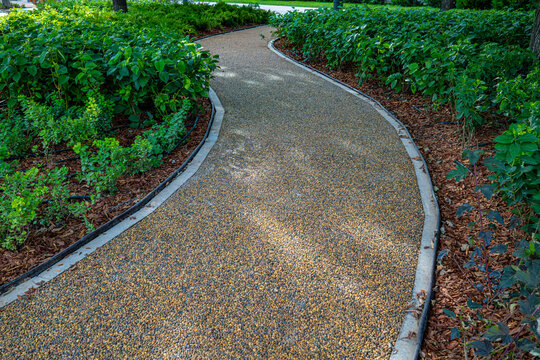 Curved pedestrian gravel path through green garden landscape with plants and shrubs, urban park design and nature concept