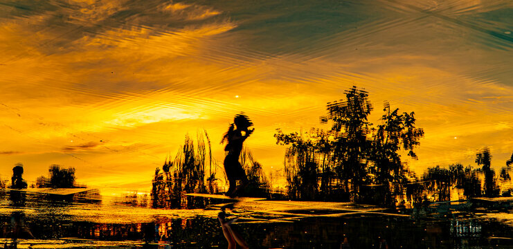 Silhouette of a girl standing by reflective water surface at dramatic golden orange sunset, nature and travel concept
