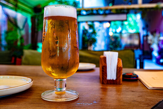 Glass of cold craft beer on wooden table in modern restaurant interior with bokeh background, bar and hospitality concept