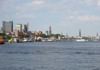 Fototapeta premium The skyline of Hamburg, Germany, viewed from river Elbe with various landmarks of the city, including the port of Hamburg, the St. Pauli landing bridges, and the bell towers of the main churches 