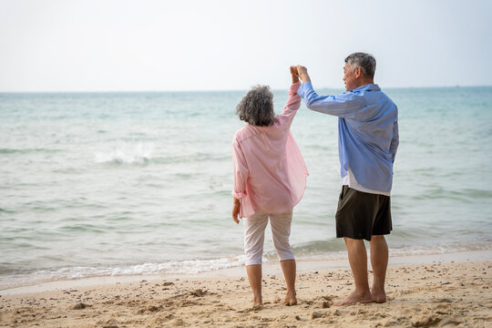 Happy Senior Asian Couple Dancing Joyfully on the Beach, Retirement Travel Lifestyle
