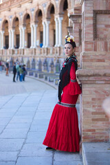 Obraz premium A beautiful woman dancing flamenco in a square in Seville, Spain. She is wearing a red ruffled dress and a flower in her hair, posing for the photo. Flamenco, a UNESCO Intangible Cultural Heritage.
