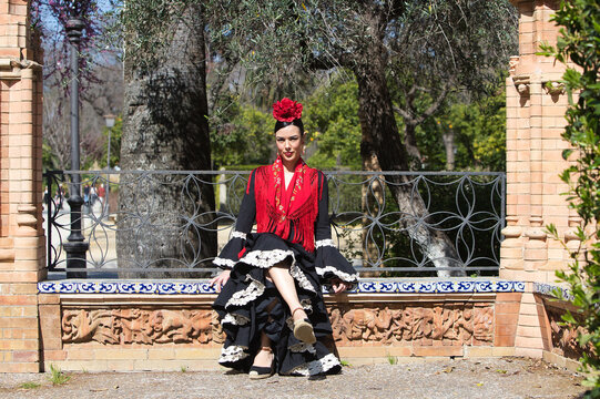 A beautiful flamenco dancer sitting on a tiled bench in a square in Seville, Spain. She is wearing a black ruffled dress and a shawl. Flamenco, a UNESCO Intangible Cultural Heritage.