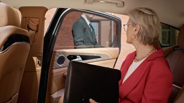 Senior Caucasian businesswoman sitting in luxury car backseat, exiting as professional chauffeur opens door. Ideal for corporate travel and executive transport videos