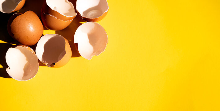 Broken eggshells scattered on yellow background with copy space