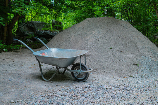 Wheelbarrow next to large pile of gravel on construction site with green forest background, landscaping and building concept