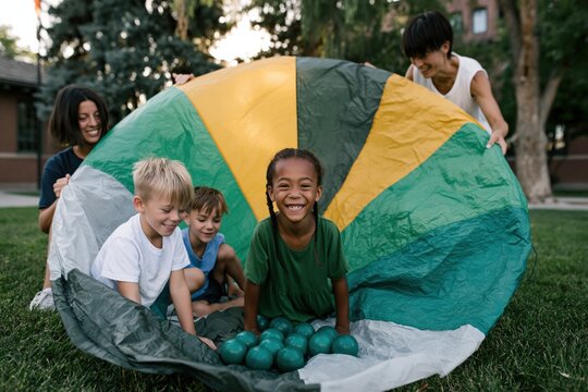 Children playing with colorful parachute and plastic balls outdoors for summer activity poster and playground background