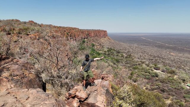 Cinematic aerial footage of a massive red sandstone escarpment towering over the dry, flat savanna plains in Namibia, Africa. Epic geological landscape.
