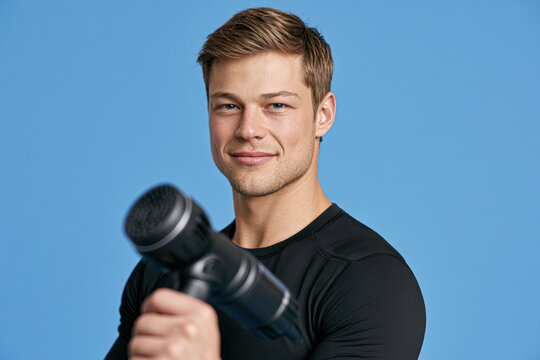 Man holding a massage gun, demonstrating muscle therapy or recovery against a blue background.