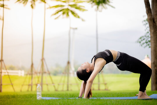 Young Asian woman practicing yoga outdoors in green park at sunrise