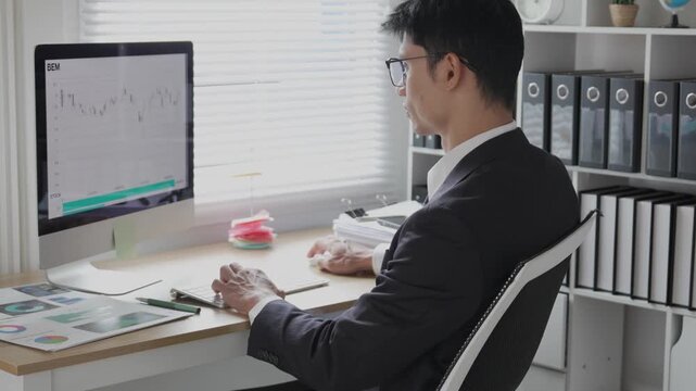 A young professional is examining investment data graphs and charts, analyzing financial information, and monitoring stock market trading reports.