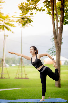 Young Asian woman practicing yoga outdoors in green park at sunrise