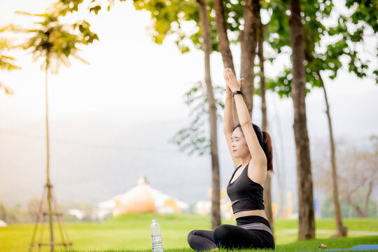 Young Asian woman practicing yoga outdoors in green park at sunrise
