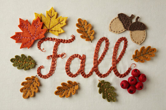 Handmade fall embroidery on white fabric, autumn leaves and acorns felt craft, seasonal textile art with red berries and cursive lettering