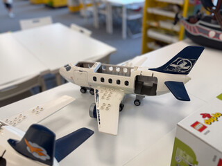 Fototapeta premium Lego-style toy airplane model on a table in a classroom or workshop, with blurred building area in the background