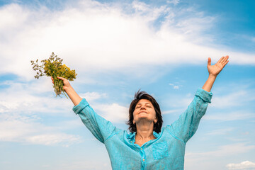 Obraz premium Woman standing in green field with her arms outstretched, facing sun, embracing happiness and beauty of nature. Women's mental health, accepting one's age