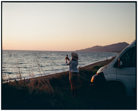 Woman photographing with smartphone at sunset, shot on film 