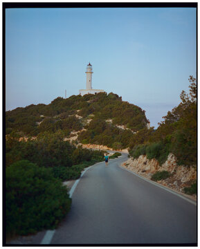 Anonymous runner on the winding road toward lighthouse in Greece, film