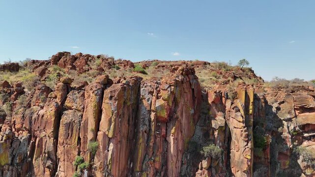 Cinematic aerial footage of a massive red sandstone escarpment towering over the dry, flat savanna plains in Namibia, Africa. Epic geological landscape.