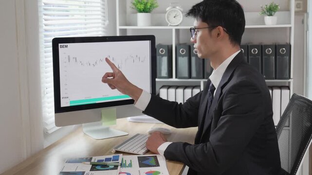 A young professional is examining investment data graphs and charts, analyzing financial information, and monitoring stock market trading reports.