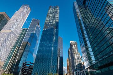 Fototapeta premium Low angle view looking up at the tall skyscrapers of Hudson Yards in midtown Manhattan, showcasing modern glass facades and futuristic architectural design.