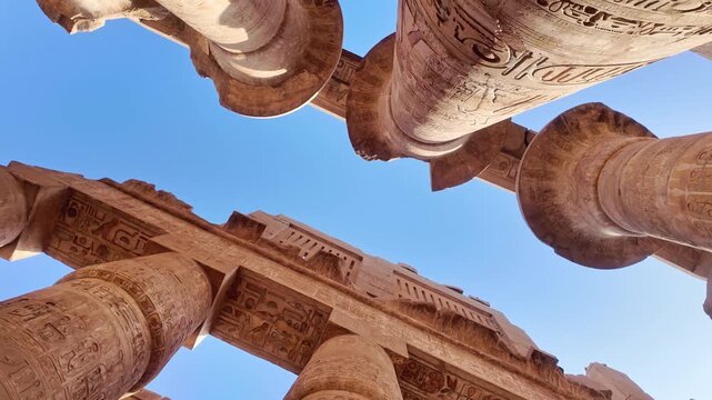 rolling shot of Impressive low angle perspective moving through the monumental papyrus columns of the great hypostyle hall at karnak temple complex in luxor