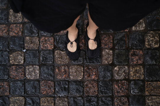 Woman standing on wet cobblestone street wearing black shoes