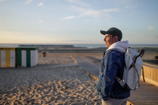 Man with backpack looking at the ocean from a beach boardwalk