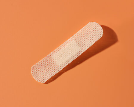 A band aid against an orange background with drop shadow