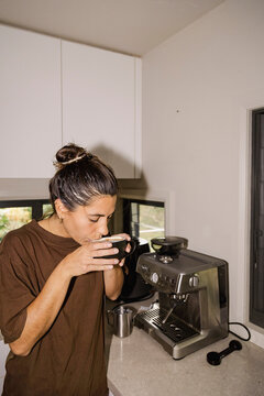 Woman sipping morning coffee beside espresso machine at home UGC