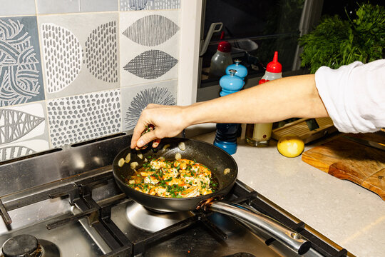 Adding herbs to prawns in pan for homemade seafood dinner
