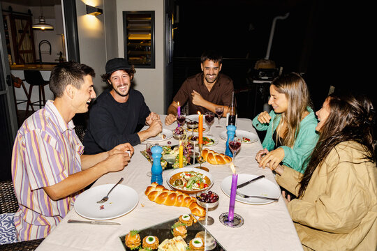 Friends laughing around candlelit dinner table at home