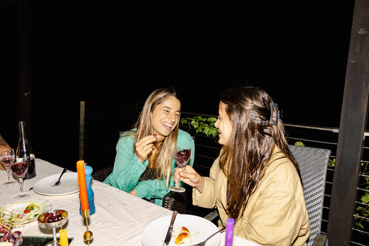 Two women laughing over wine at outdoor dinner party