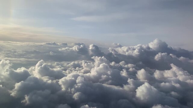 High-altitude aerial view of expansive cumulus clouds with bright tops and shadowed undersides, pale blue sky with wispy cirrus clouds near horizon, diffuse sunlight.