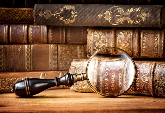 Old books and antique magnifying glass on a wooden background. An ancient book and magnifying glass as a symbol of history, education. Translation of book titles - history of England.