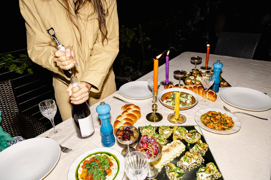 Opening wine beside candlelit appetizers at a dinner party with flash