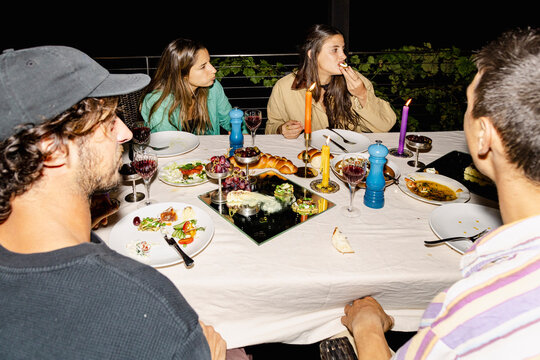Friends eating and talking around outdoor dinner table