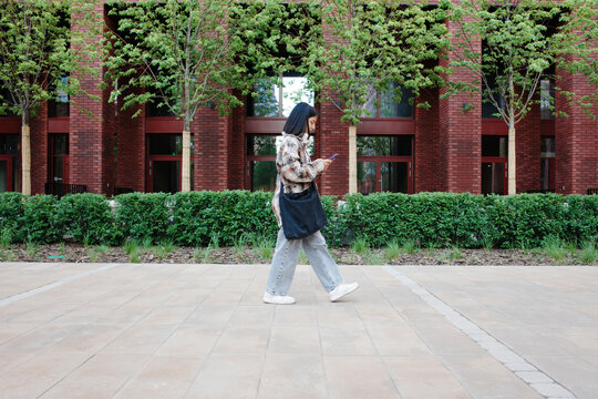 Student walking on university campus using smartphone