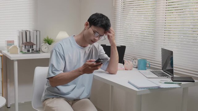 An Asian man, looking stressed about household finances, slumps down in his living room, showing signs of worry.