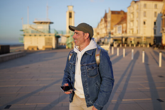 Man holding smartphone while walking on a coastal promenade