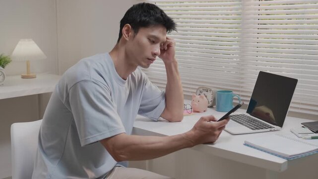 An Asian man, looking stressed about household finances, slumps down in his living room, showing signs of worry.