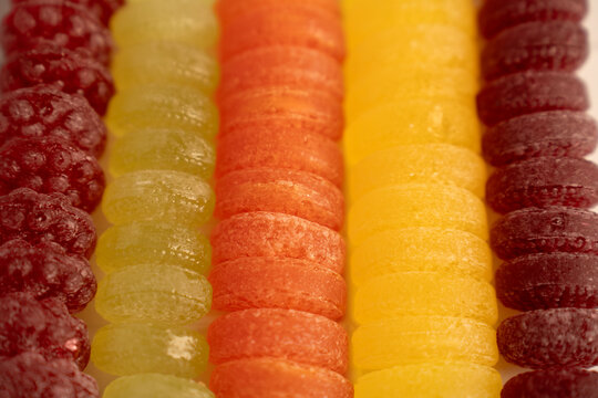 macro closeup of colorful sugarcoated gumdrops and jelly candies arranged in neat vertical rows, showcasing vibrant red, green, orange, yellow and purple hues, texture and shallow depth, fruitflavor