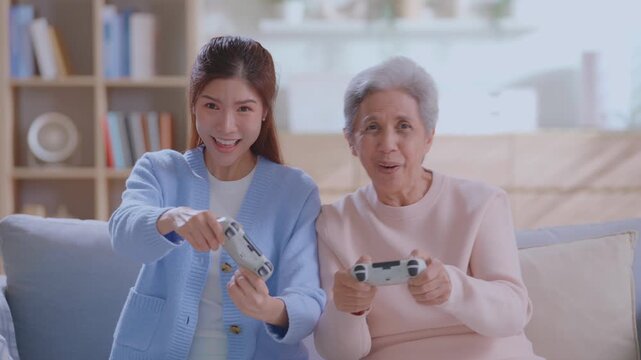 Happy senior mother and adult daughter playing video games together on a sofa at home.  intergenerational fun, gaming, living room leisure, and modern retirement lifestyle.  family bonding Concept