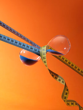 Hourglass with blue sand and measuring tapes symbolize time